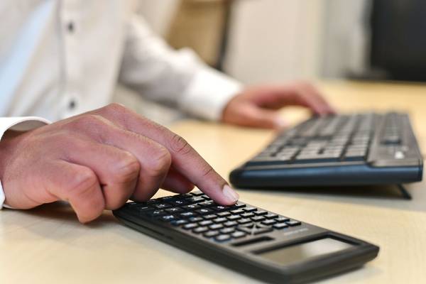 Benjamin Colin Köpper sitzt an einem Schreibtisch und tippt auf einem Taschenrechner, während seine andere Hand auf der Tastatur ruht.