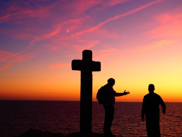 Menschen stehen bei Kreuz vor Sonnenuntergang